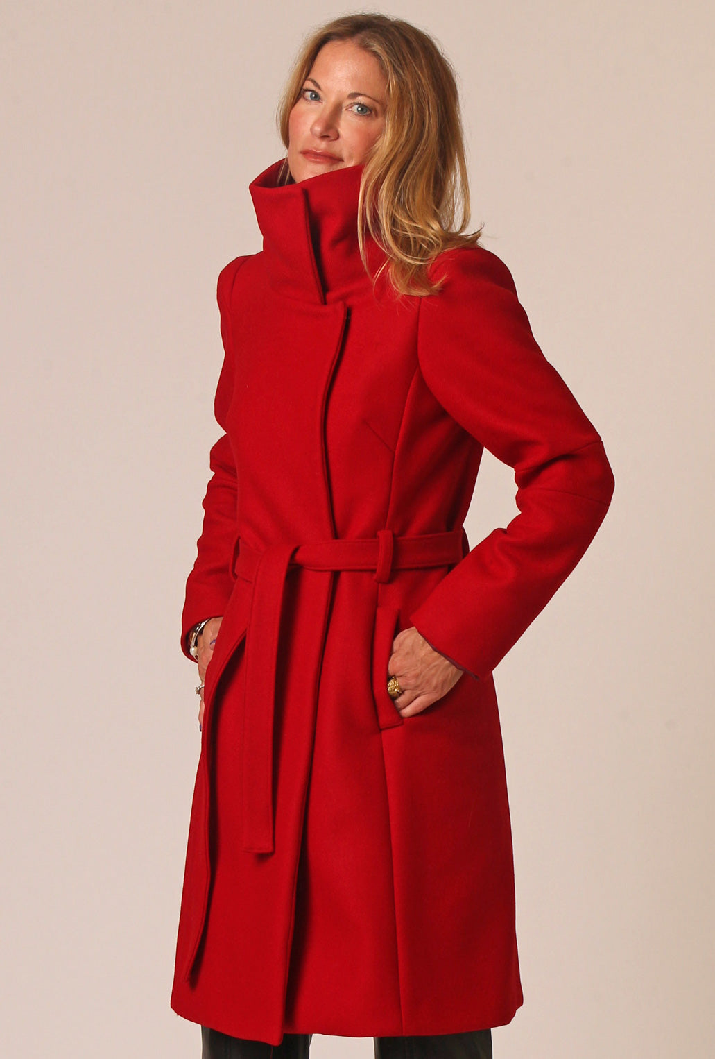 Woman wearing tall collar, knee length twill wool trench coat with defined shoulders and tie belt